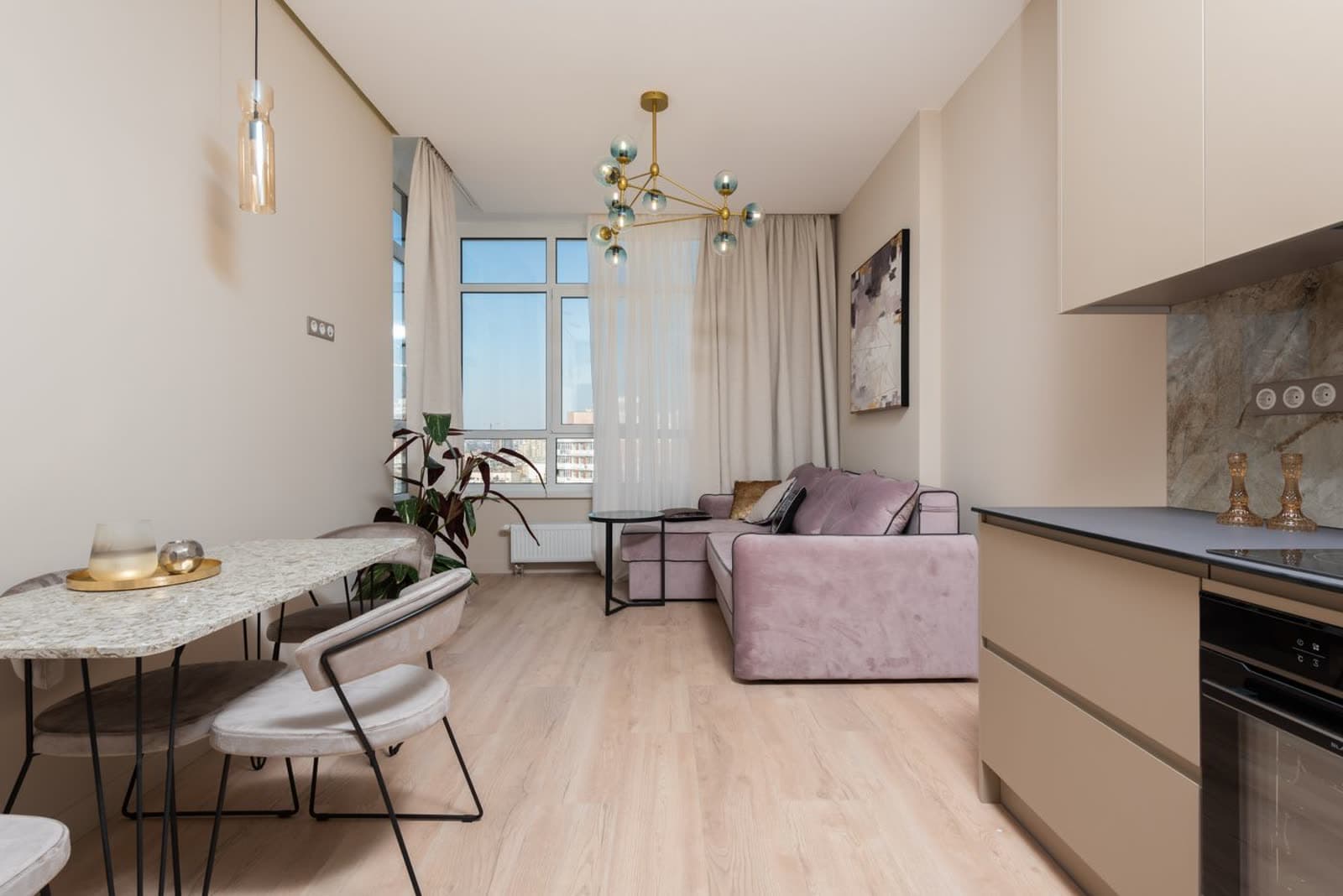 Apartamento compacto pronto e decorado, com sala integrada à cozinha, sofá rosé e janela ampla para a cidade