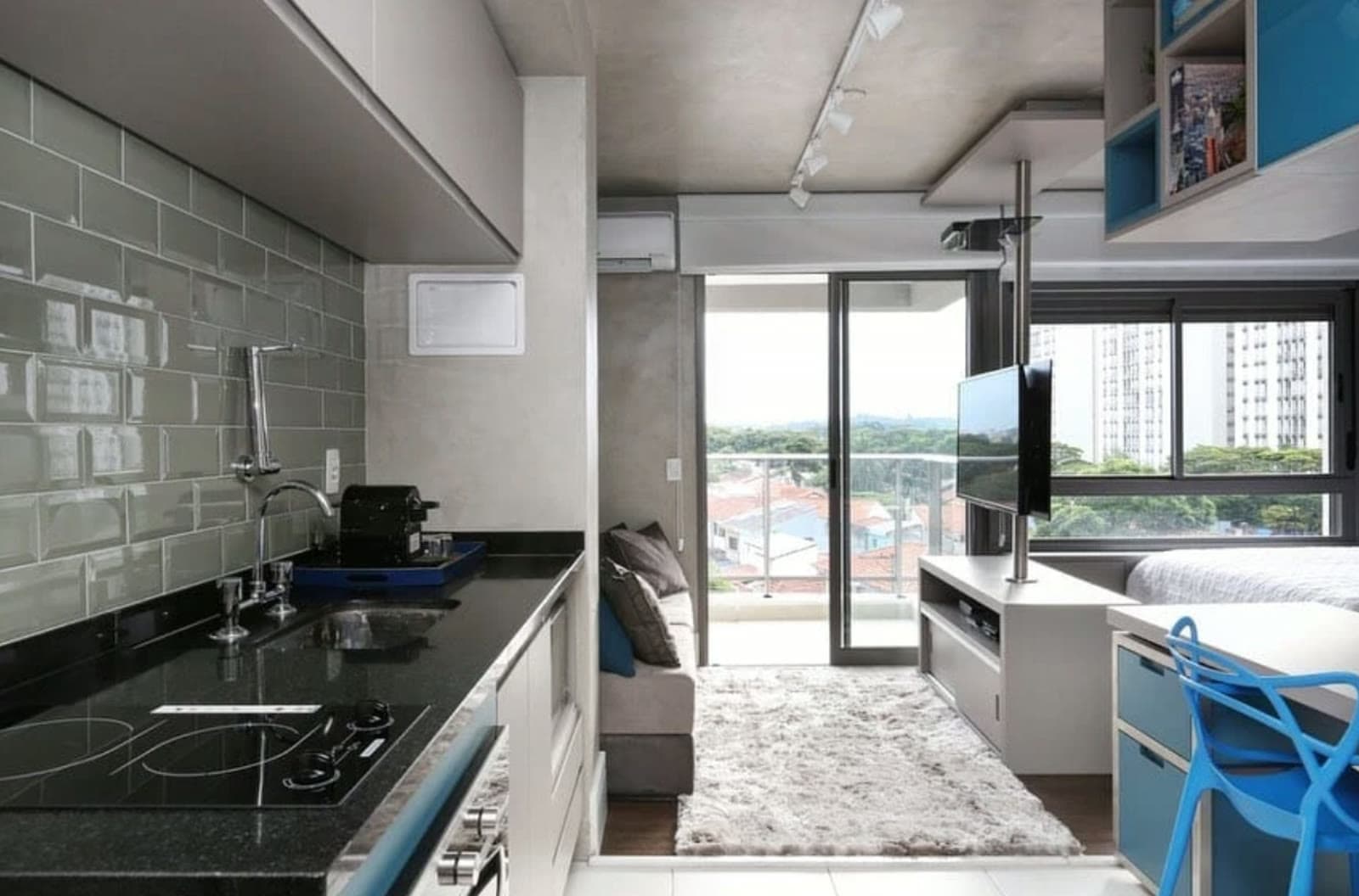 Studio decorado com cozinha, sala integrada e varanda com vista para casas, árvores e prédios de São Paulo